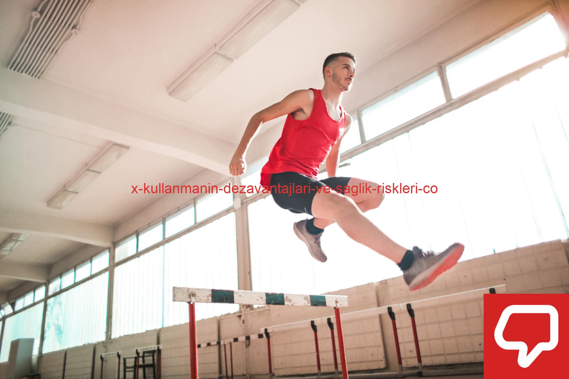 A young male athlete in a red outfit jumps over a hurdle indoors, showcasing agility and determination.