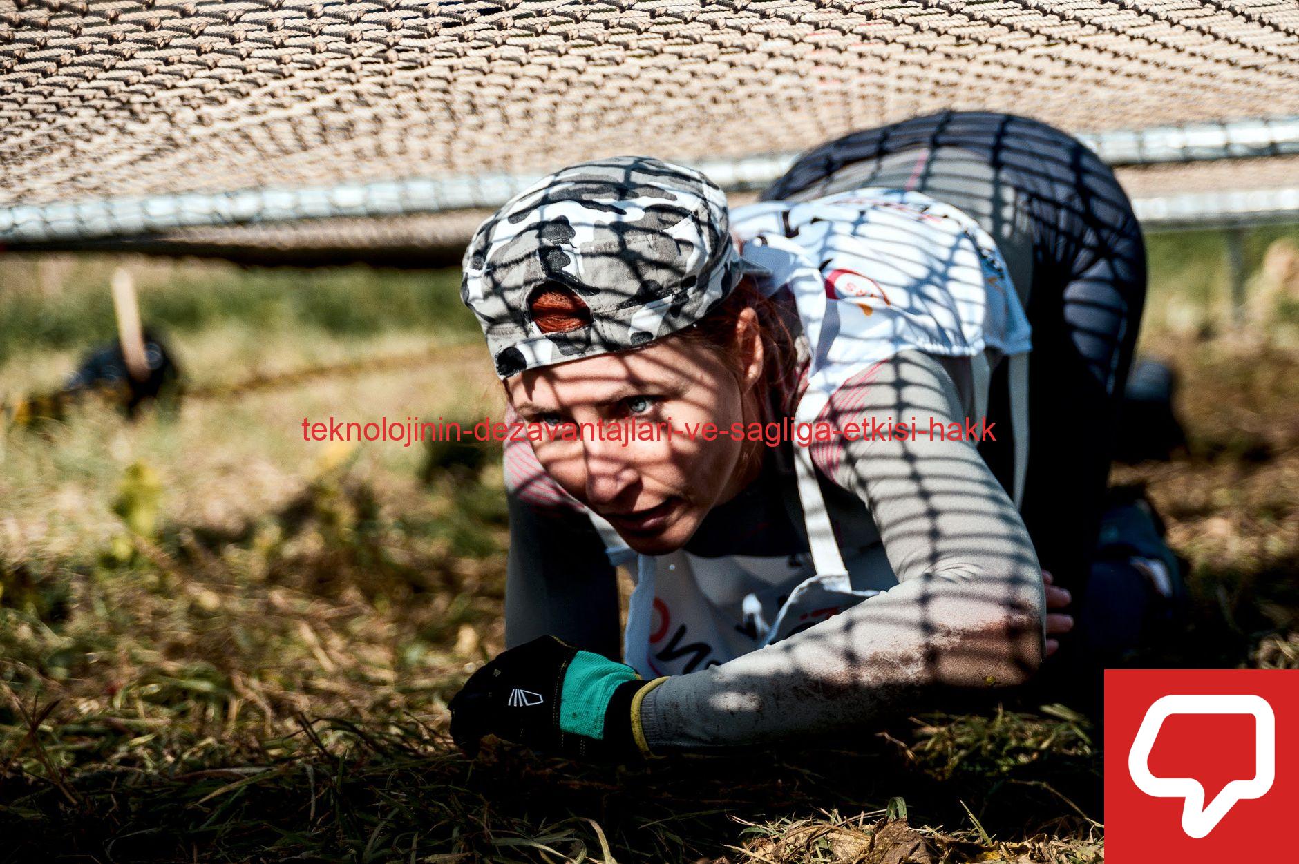 A young woman crawls under a net in an outdoor training or obstacle course.